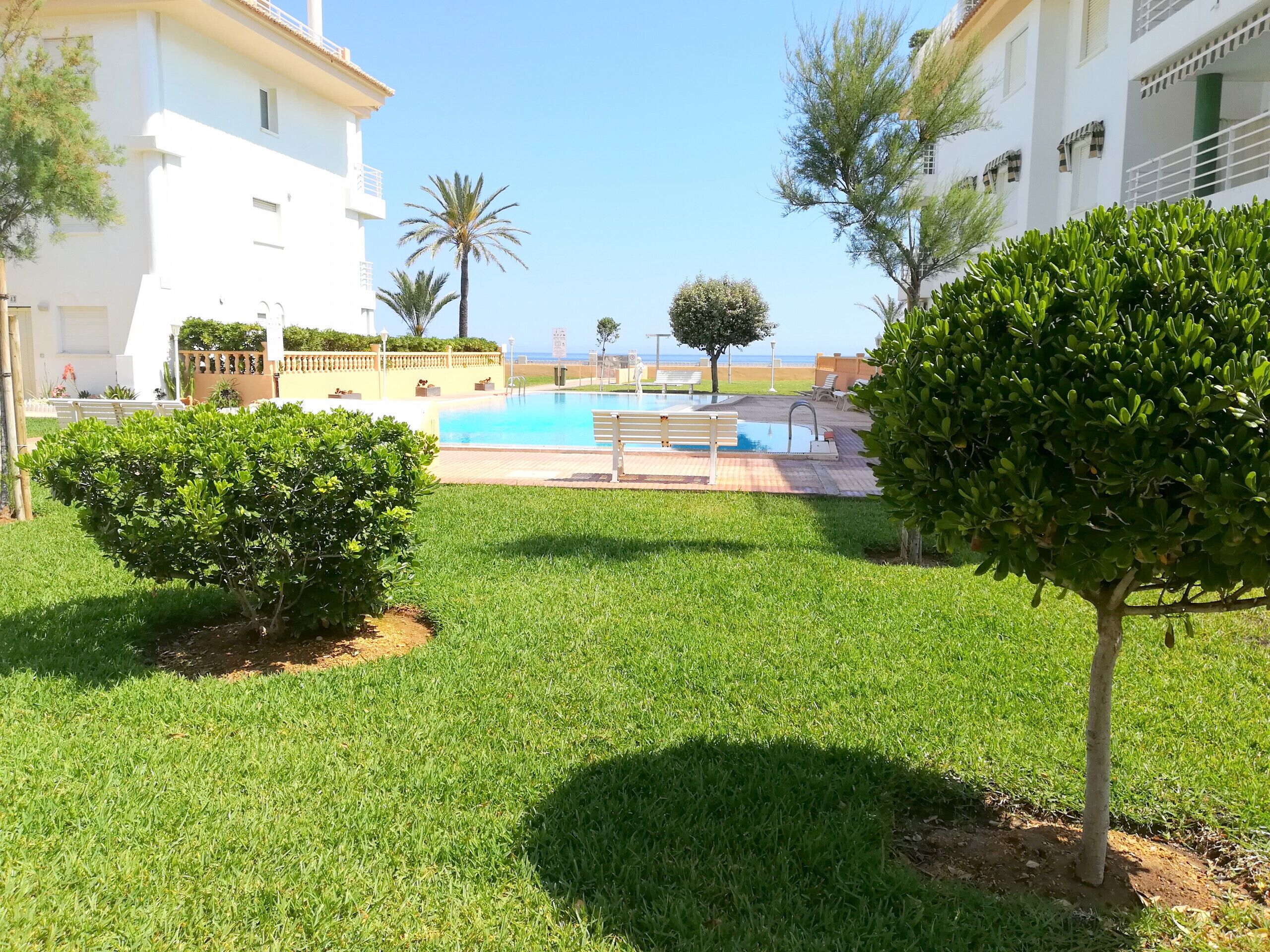 Un área de piscina con vista despejada al mar, rodeada de césped y árboles bien cuidados.