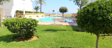 Un área de piscina con vista despejada al mar, rodeada de césped y árboles bien cuidados.