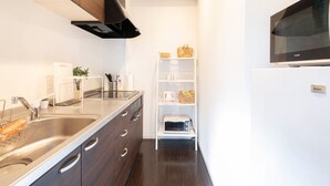 A modern kitchen with dark wood cabinets, stainless steel appliances, and a white shelving unit with kitchen items. - nid NIPPONBASHI at Ebisu (Osaka)