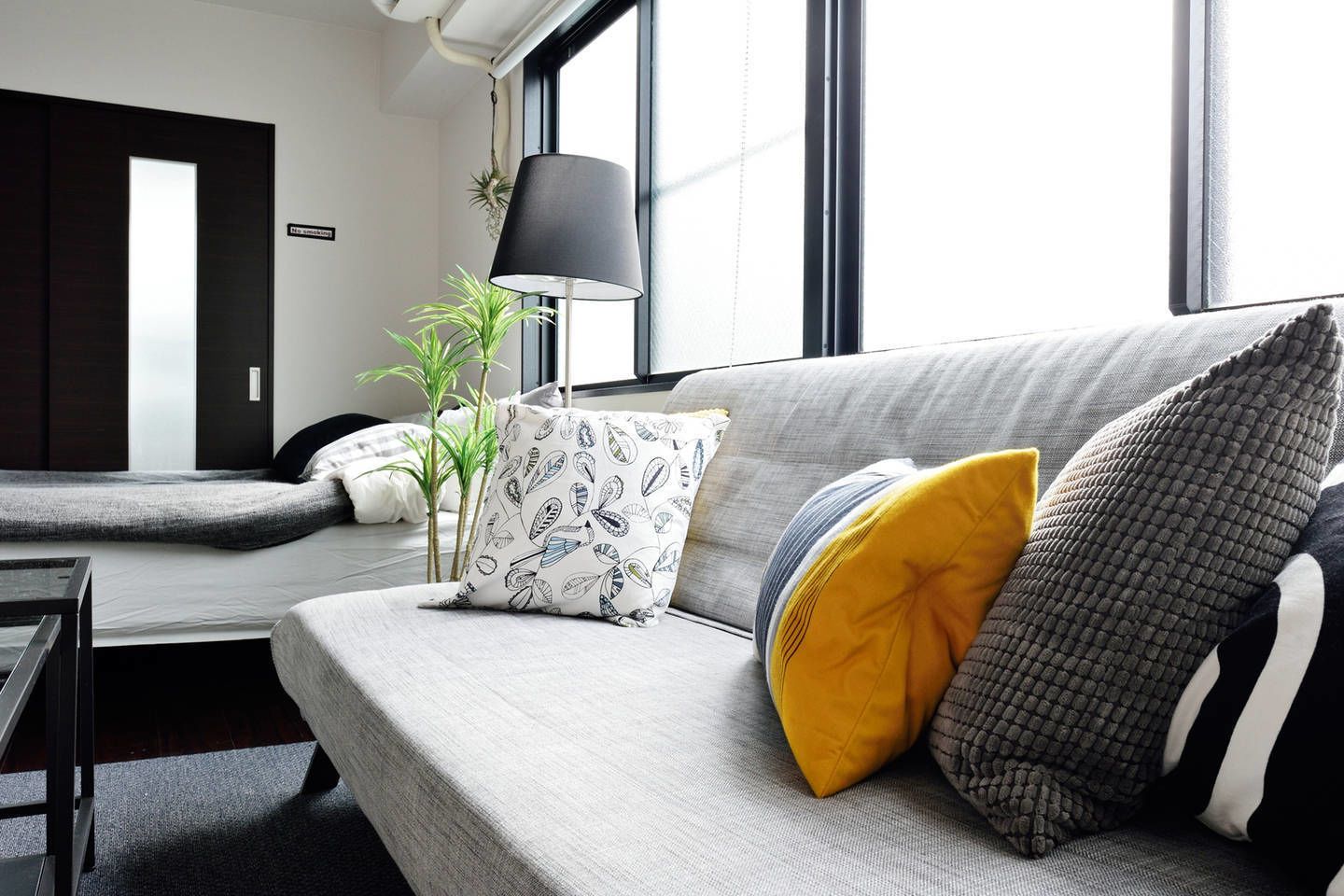 A modern living room with a sofa, pillows, a lamp, and a plant.