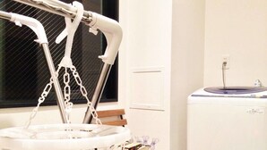A room with a crib, a small wooden table, a washing machine, and a window with blinds. - nid NIPPONBASHI at Ebisu (Osaka)