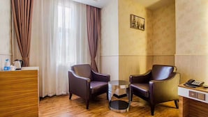 Habitación de hotel con dos sillones de cuero, una mesita redonda pequeña, un escritorio de madera y un teléfono.