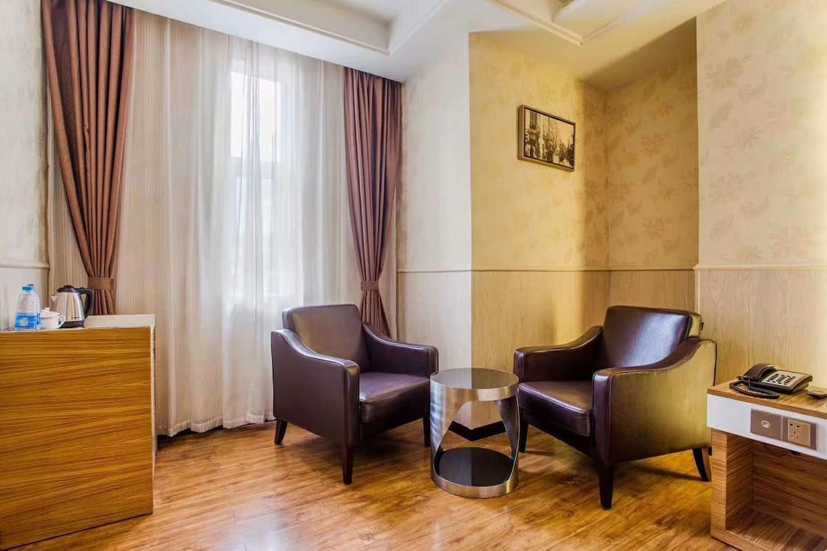 A hotel room with two leather armchairs, a small round table, a wooden desk, and a telephone.