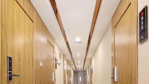 Un pasillo de hotel con puertas de madera, alfombra estampada y un cartel con números.