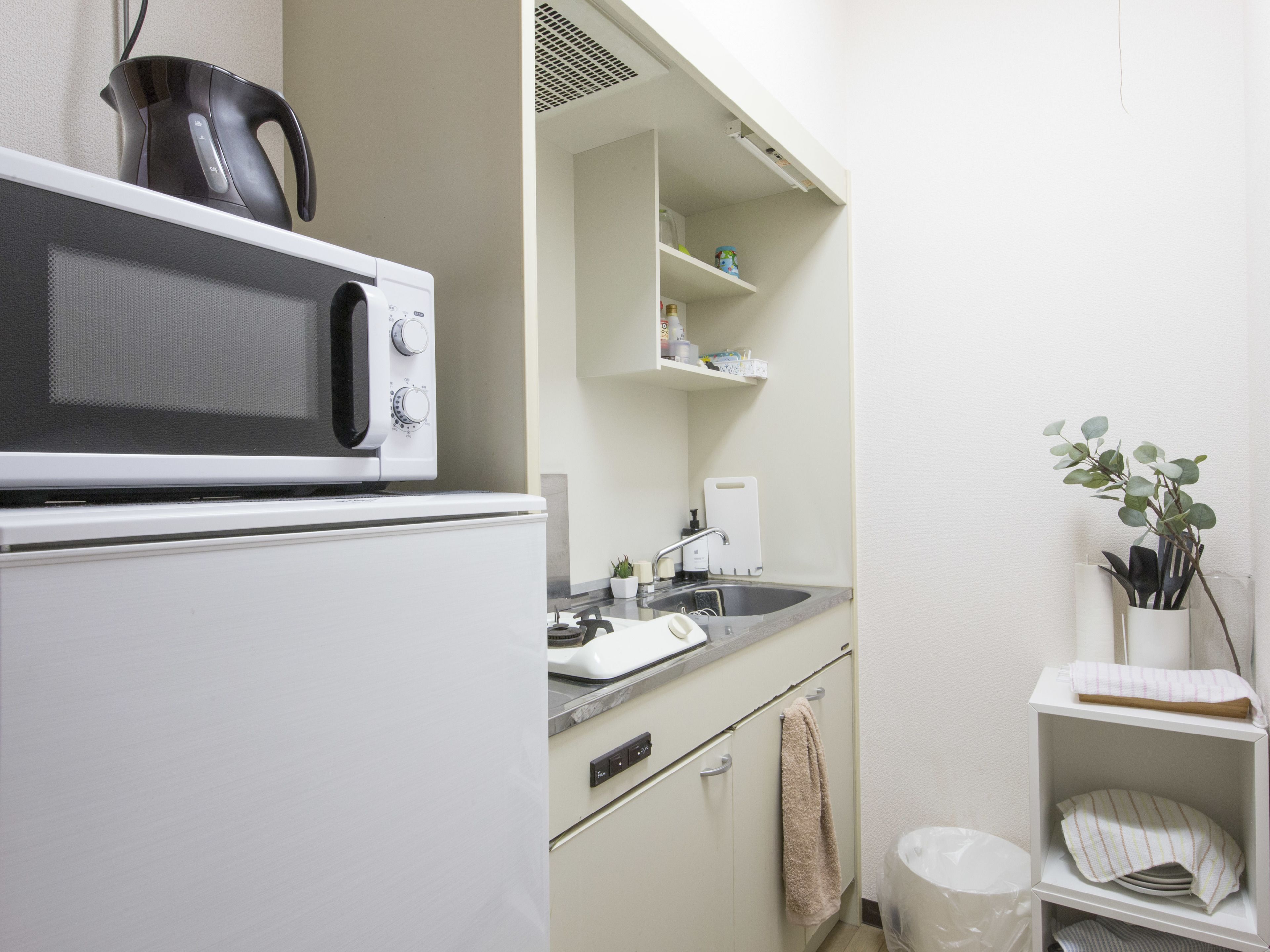 A compact kitchen with a microwave, kettle, and sink.