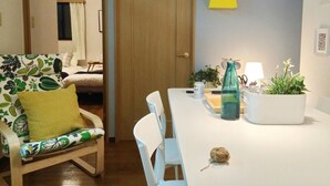Un comedor con una mesa blanca, sillas, un cojín amarillo, un florero verde y una planta en maceta.