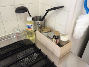 Eine Küchenarbeitsplatte mit verschiedenen Gegenständen, darunter eine Flasche Kochöl, ein Sieb, eine Holzkiste mit Gläsern und ein schwarzes Gerät.