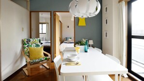 Una habitación de hotel moderna con zona de comedor, un ventanal grande y una lámpara de techo original.