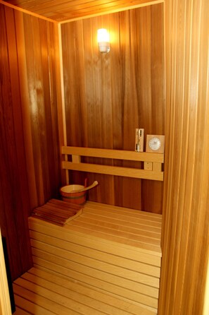 A wooden sauna with a bench, a wooden shelf with a clock, and a wall-mounted light.