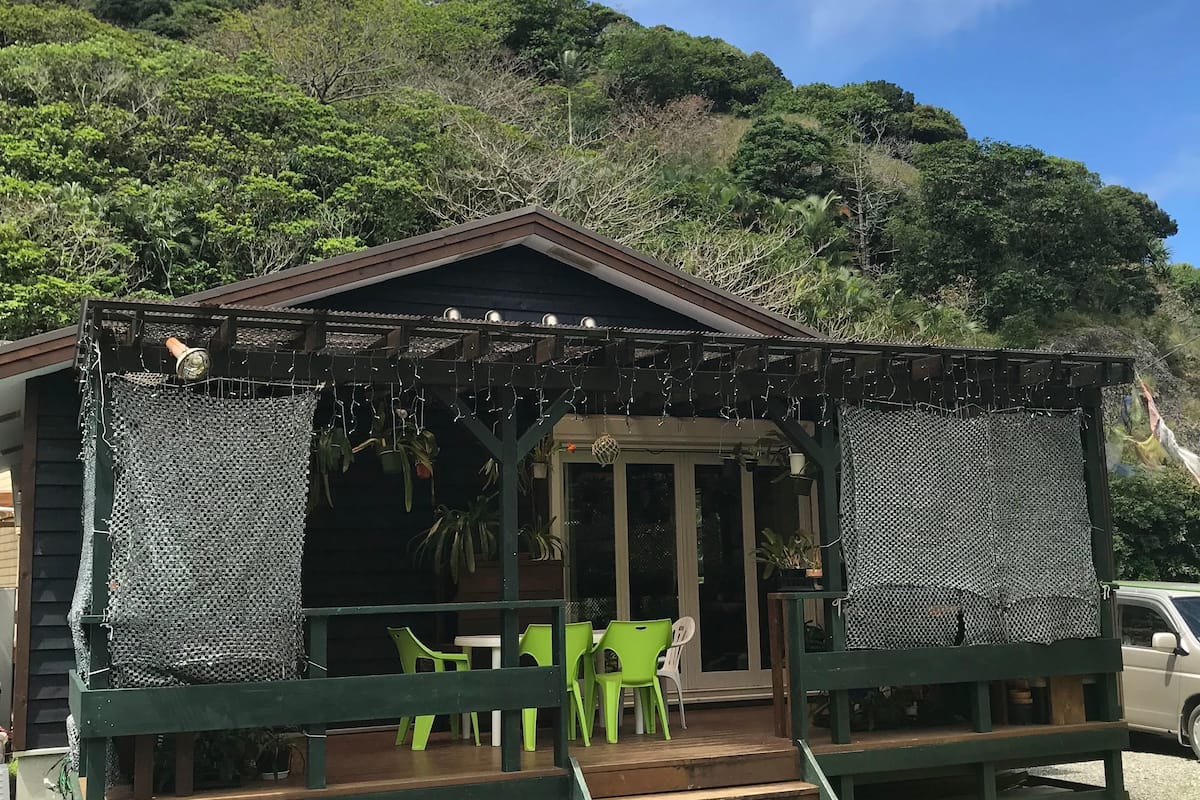 Une cabane en bois rustique, dotée d’une véranda, de chaises en plastique vertes et d’une table de pique-nique.