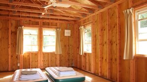 Una habitación con paredes y suelos de madera, dos camas individuales con colchones y cortinas en las ventanas.