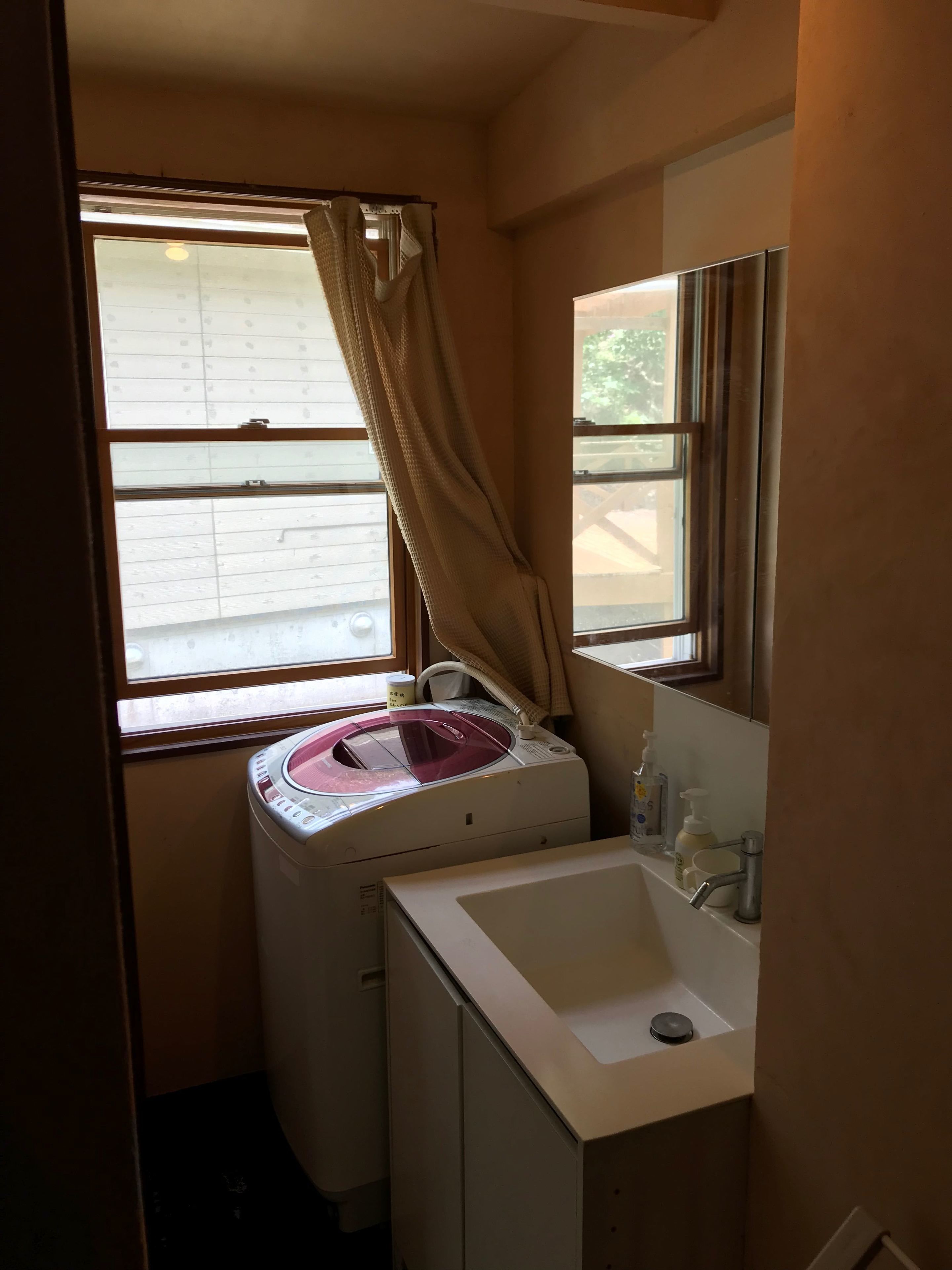 Un baño pequeño con lavadora, un lavabo y una ventana con cortinas.