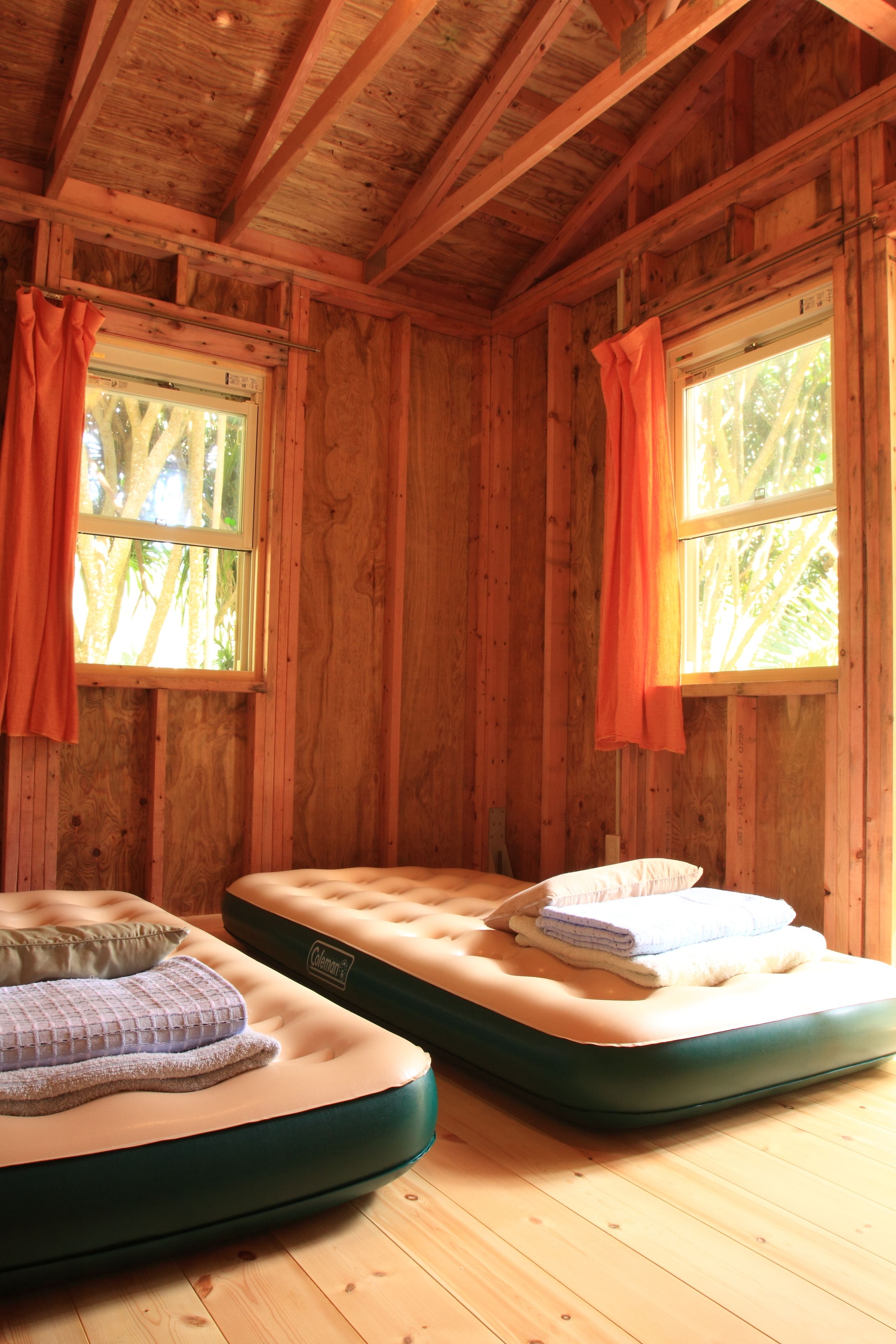 A cabin with two bunk beds, wooden walls, and windows with curtains.