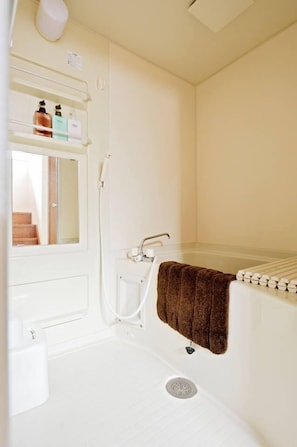 Ein kleines, weißes Badezimmer mit einer Dusche, einem Handtuch an der Wand und einem Ablagefach mit Toilettenartikeln.