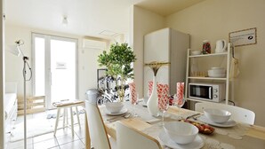 A dining area with a table set for four, white chairs, a white cabinet, and a microwave on the counter. - nid Shimanouchi House (Osaka)