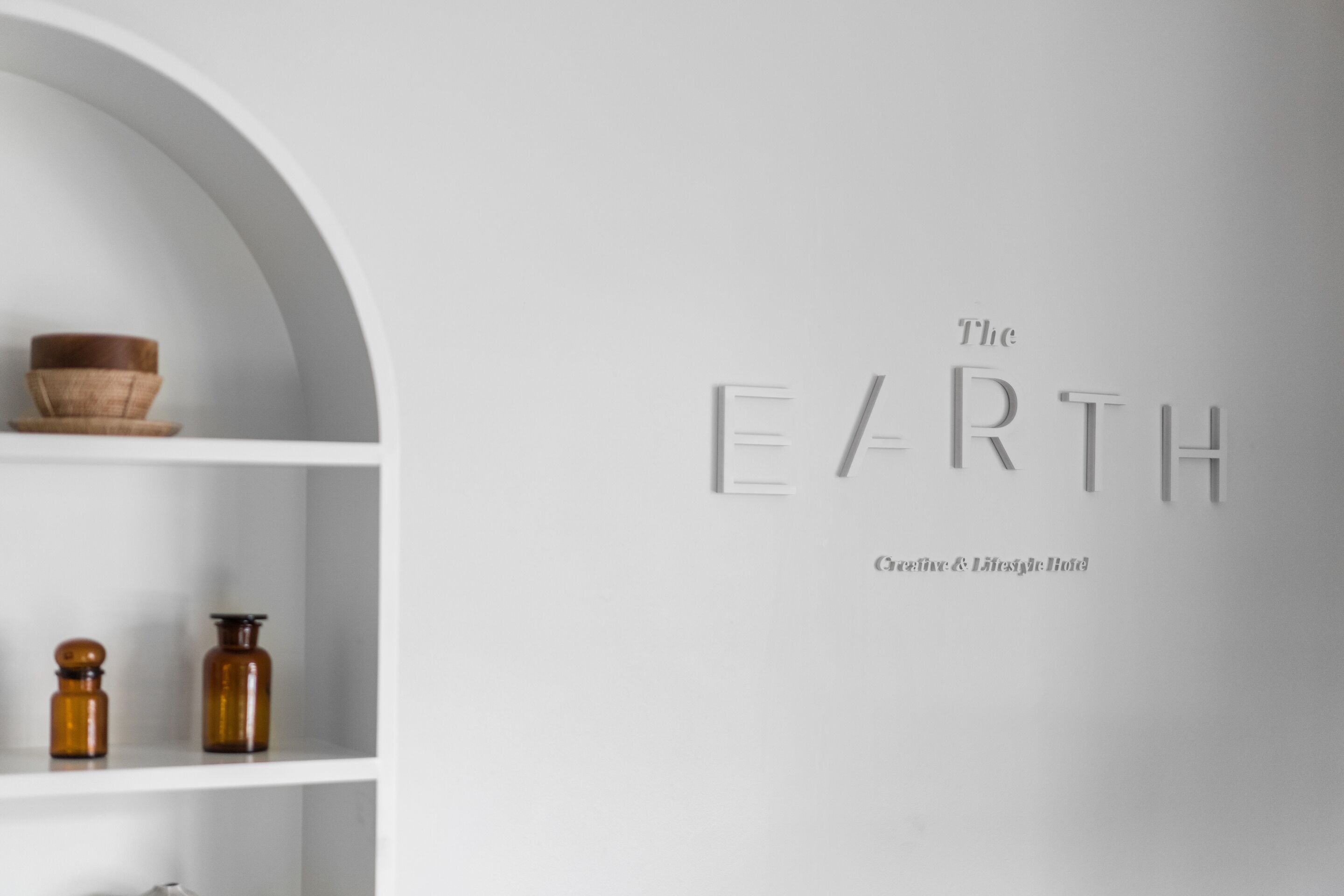 Un intérieur minimaliste avec une étagère blanche où sont exposés un bol et deux bouteilles. Sur le mur, on peut lire le texte suivant : « The EARTH, une marque créative axée sur le style de vie. »