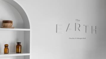 Un intérieur minimaliste avec une étagère blanche où sont exposés un bol et deux bouteilles. Sur le mur, on peut lire le texte suivant : « The EARTH, une marque créative axée sur le style de vie. »