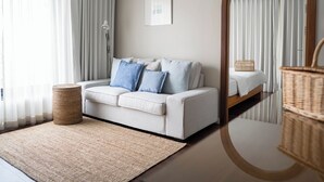 A modern bedroom with a large mirror, a sofa with blue cushions, a wicker basket, and a bedside table. - The Earth Hotel (Chiang Mai)