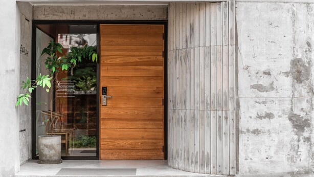 A modern entrance with a wooden door, a concrete wall, and a potted plant. - The Earth Hotel (Chiang Mai)