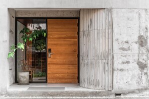 A modern entrance with a wooden door, a concrete wall, and a potted plant. - The Earth Hotel (Chiang Mai)