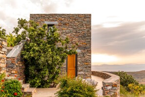 Edificio de piedra con puerta de madera, rodeado de follaje y una escalera de piedra.