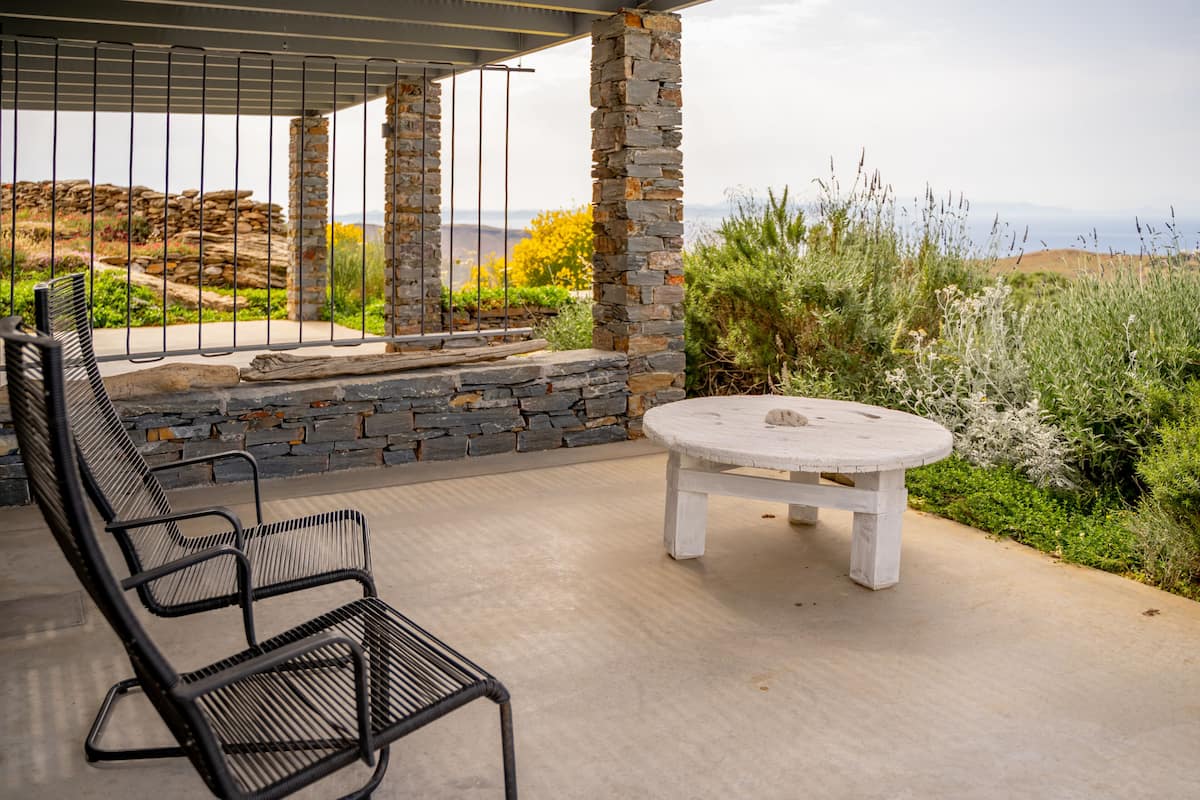 A covered patio area with a stone wall, a round table, and two black metal chairs.