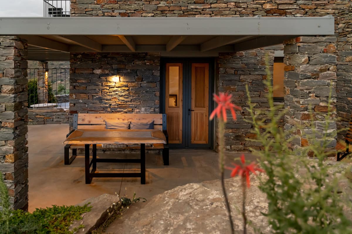 A stone exterior with a bench and table under a covered area.