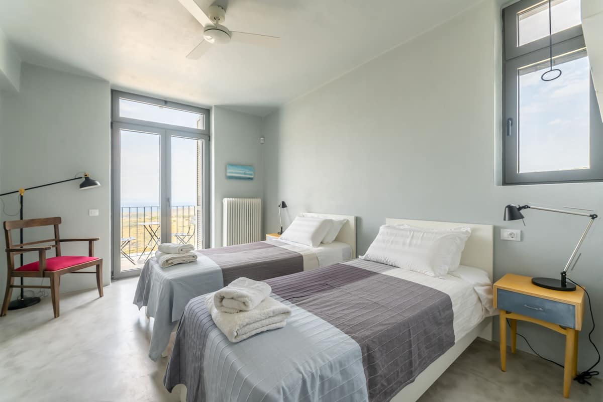 A bedroom with two beds, a chair, a nightstand, and a ceiling fan.