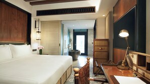 Una habitación de hotel con una cama grande, un escritorio con lámpara, una silla de madera, un ventanal y vistas al pasillo.