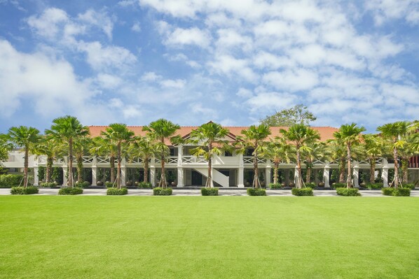 Un hotel con techo de tejas rojas, palmeras y un césped bien cuidado.