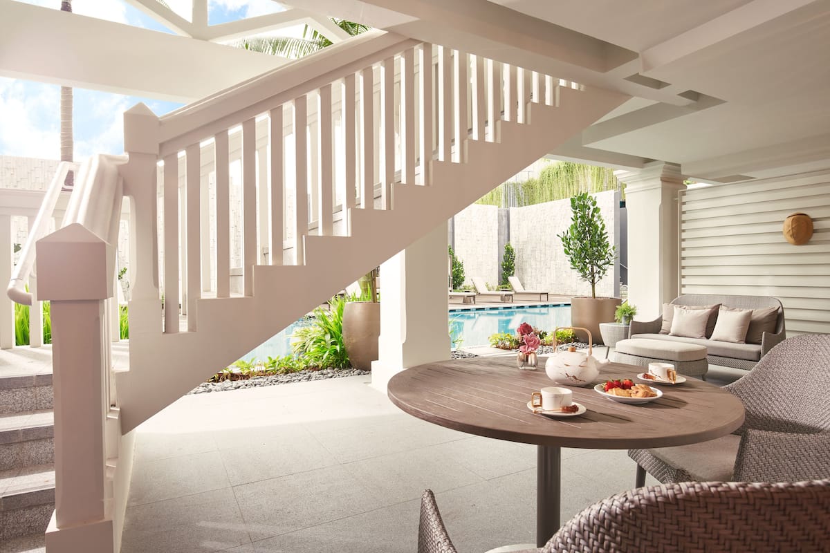 A modern outdoor patio with a round table set for tea, a white staircase, and a pool in the background.
