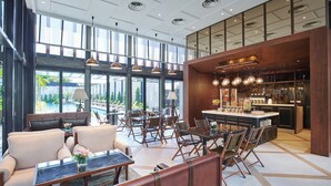 Un vestíbulo amplio con zona de bar, diferentes disposiciones de asientos y grandes ventanales con vistas al exterior.