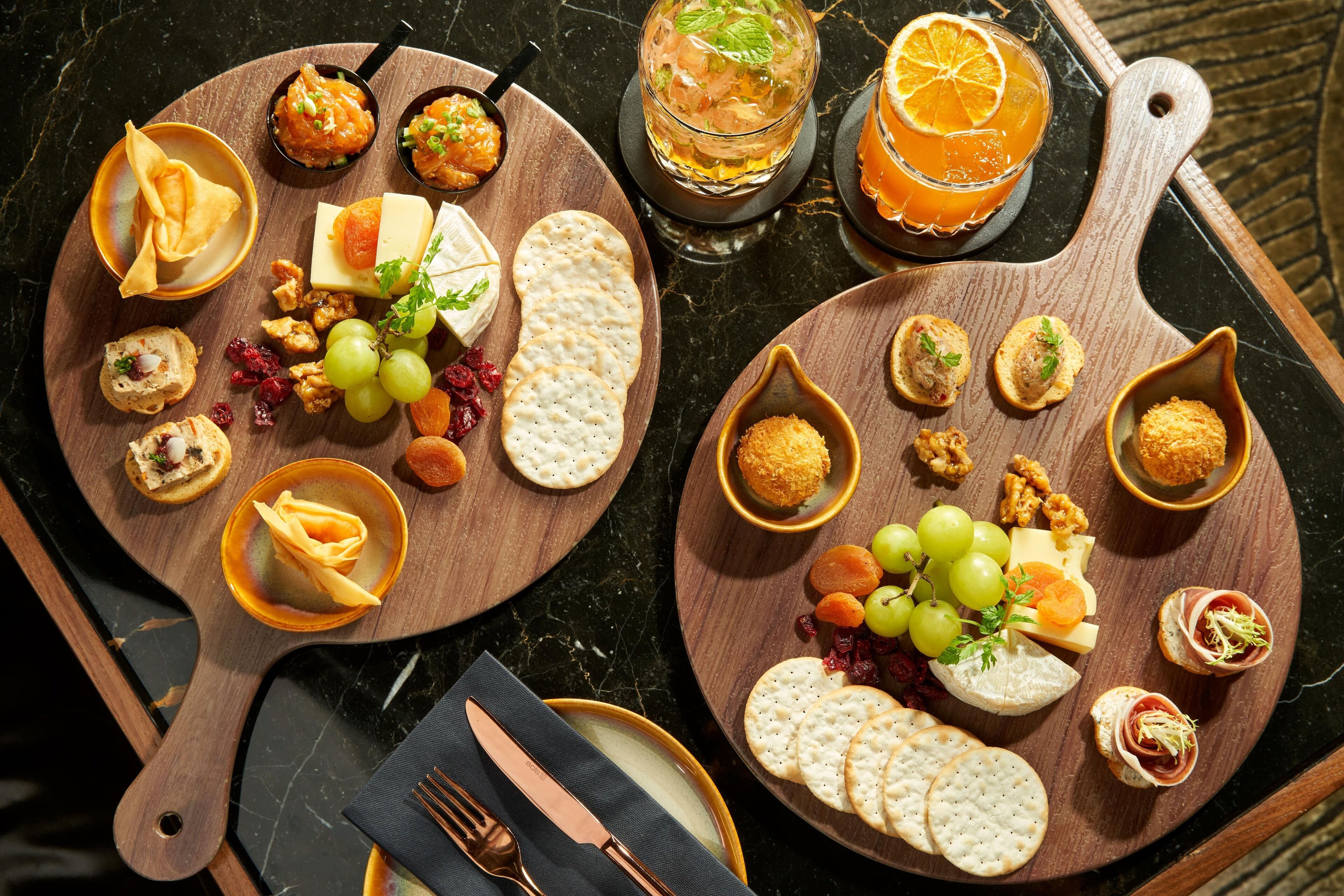 Dos tablas de madera con varios quesos, galletas y guarniciones.