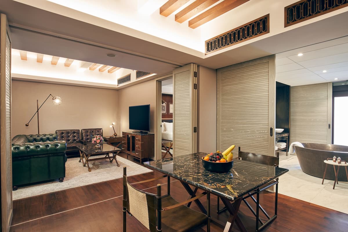A modern living room with a glass-top dining table, leather sofa, and a large window.