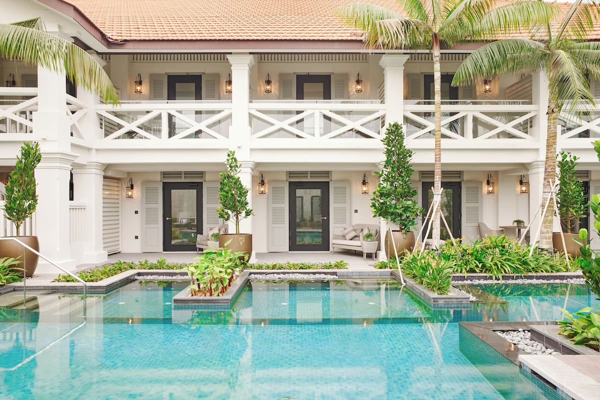 A pool area with a two-story building, palm trees, and a seating area with a sofa and chairs.