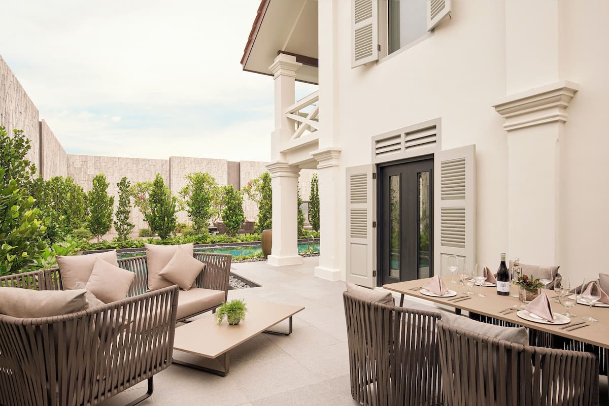 An outdoor patio with wicker furniture, a dining table set for a meal, and a pool in the background.