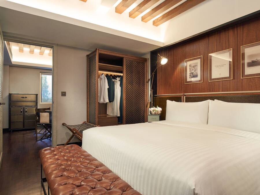 Une chambre d’hôtel avec un grand lit, un banc, une armoire et un bureau.