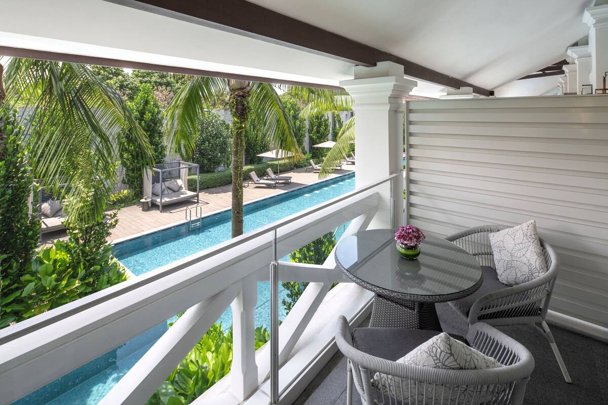 A balcony with a pool, wicker furniture, and lush greenery.