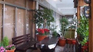 Et udendørs siddeområde med et bord og bænke, omgivet af krukker med planter og en træbænk.