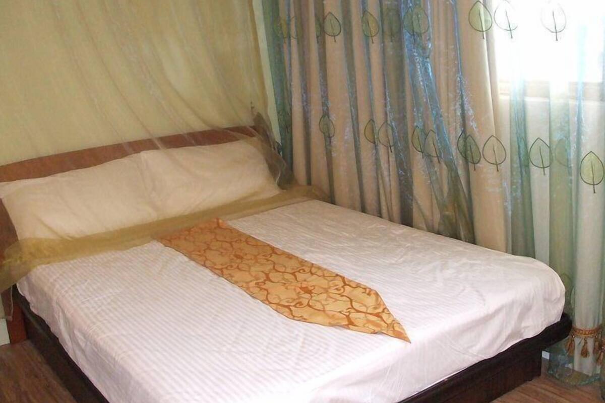 Ein Bett mit weißer Matratze, einem gemusterten Überwurf und einem hölzernen Kopfteil.