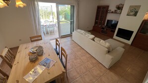 A living room with a sofa, a dining table with chairs, a TV, and a sliding glass door leading to an outdoor area.