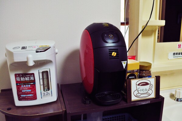 An electric kettle and a coffee machine on a wooden table with a sign indicating a free coffee.