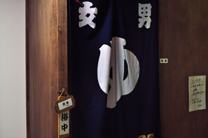 A room with a wooden door, a sign with Japanese characters, and a small hanging ornament. - Guest house HiDE (Toyako)