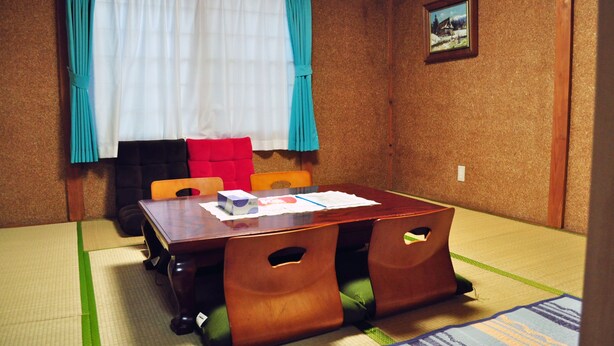 Um quarto tradicional com esteiras de tatame, uma mesa de madeira, cadeiras e um futon.