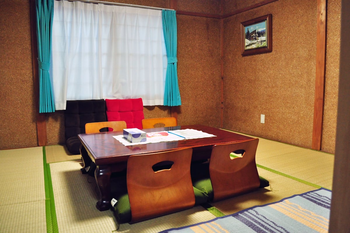 Una habitación tradicional con tatami, una mesa de madera, sillas y un futón.