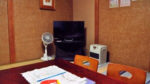 Uma sala de conferência com uma mesa de madeira, cadeiras, uma televisão, um ventilador, um ar condicionado e alguns documentos sobre a mesa.