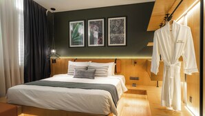 A modern hotel room with a large bed, a wooden headboard, a robe hanging on the wall, and three framed pictures above the bed. - Macalister Hotel Managed By The Ascott Limited (George Town)
