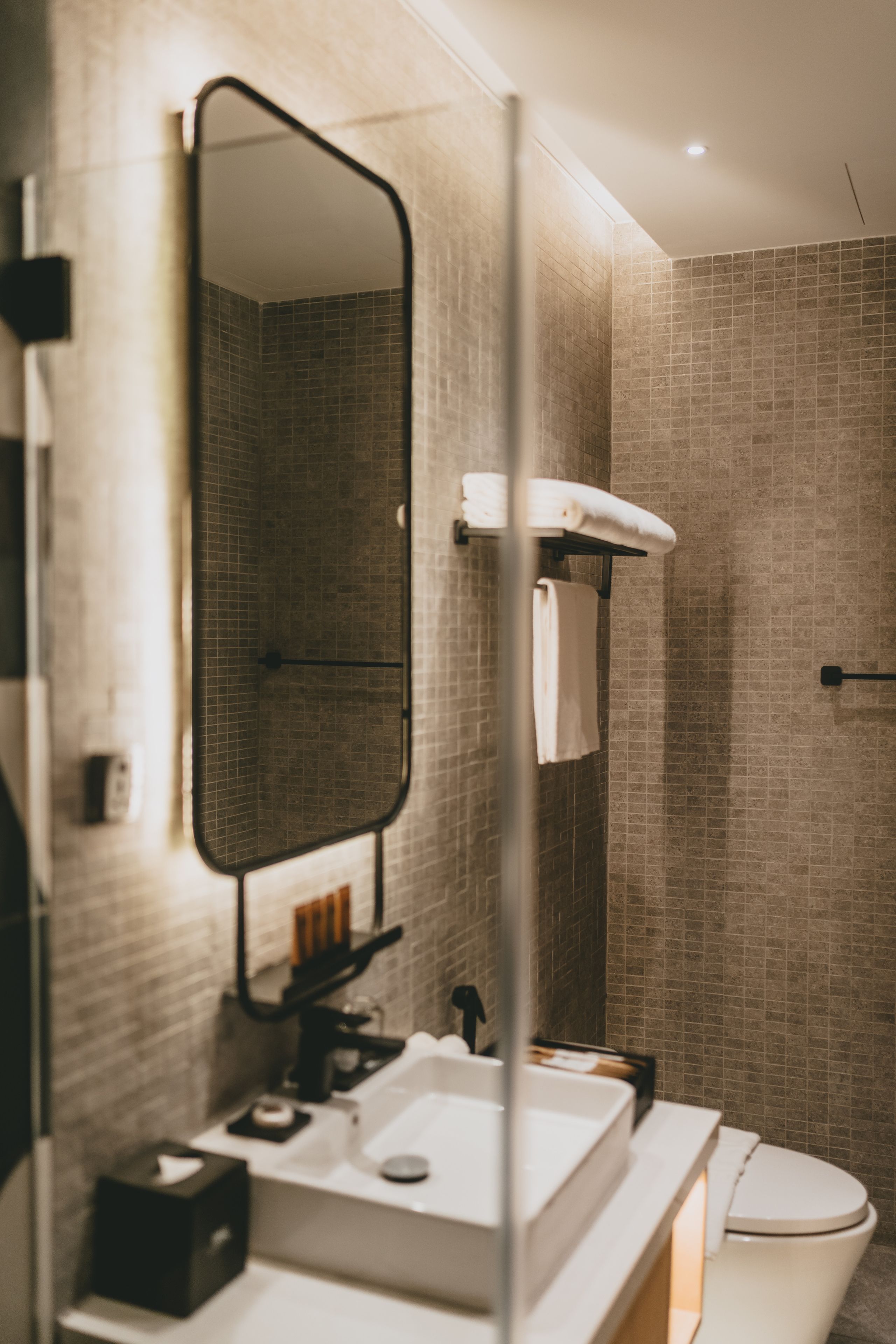 A modern bathroom with a large mirror, a white sink, a towel rack, and a shower area.