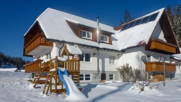 Eine zweistöckige Chalet mit Holzspielplatz und Skilift, umgeben von Schnee.