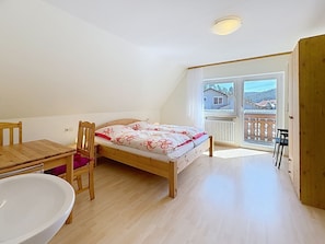 Une chambre à coucher avec un lit, un bureau en bois, une chaise, une petite table et une grande fenêtre.